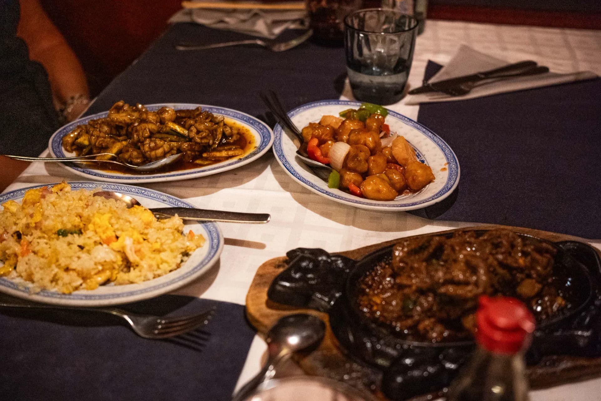 Mesa puesta con varios platos chinos compartidos: arroz, fideos y carne salteada