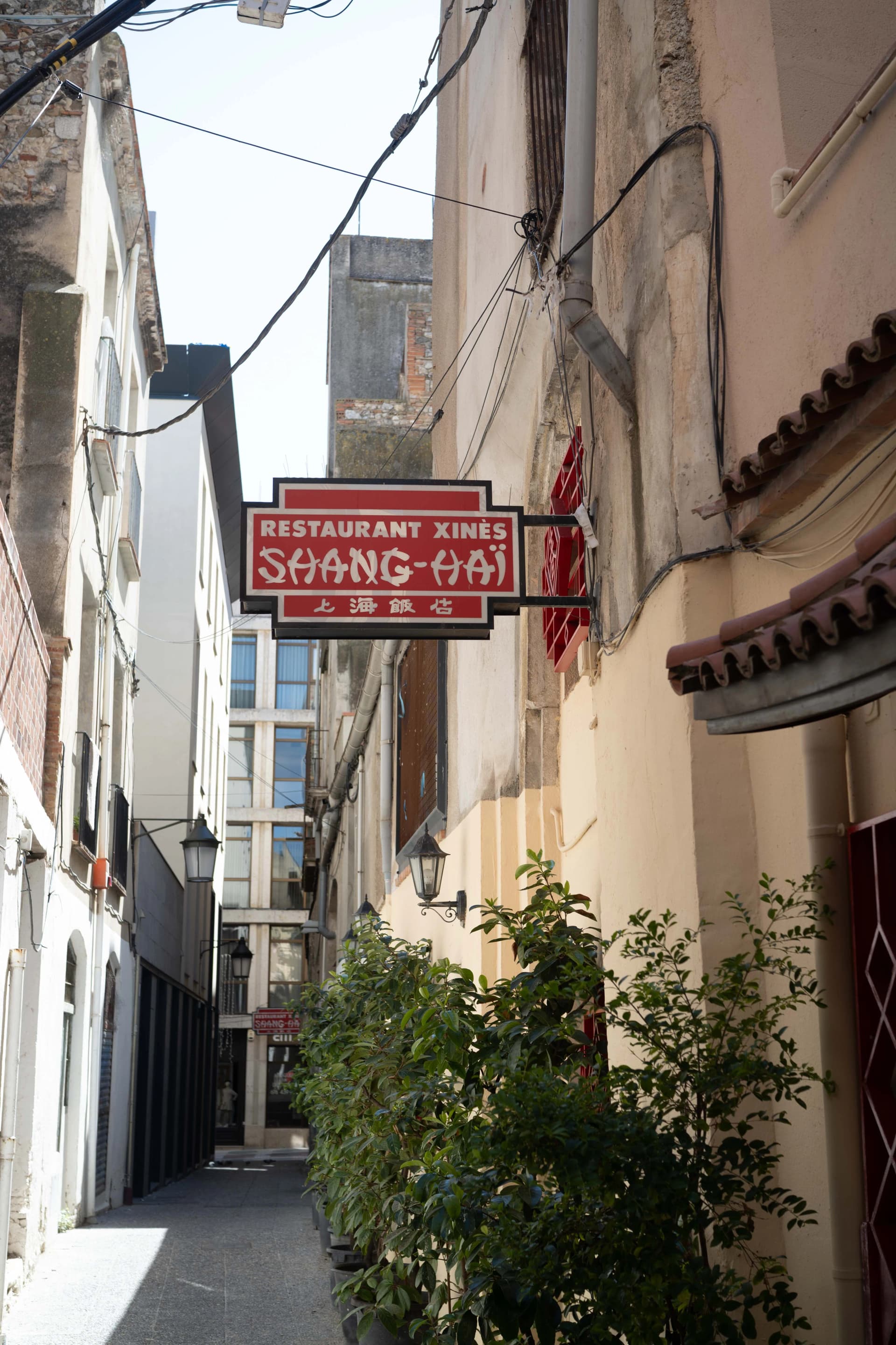 Rótulo rojo del Restaurant Xinès Shang-Haï colgado en un callejón peatonal estrecho